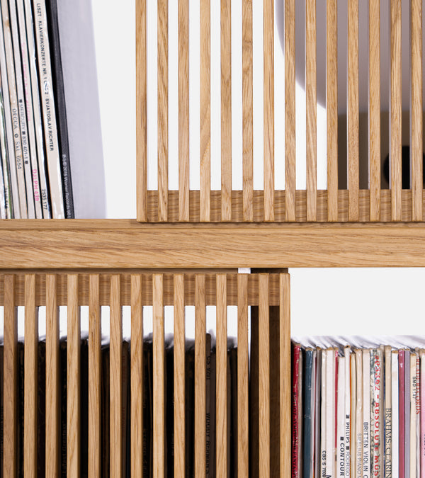 Wooden bookshelf with a modern, staggered design and slatted panel accents, set against a white background.