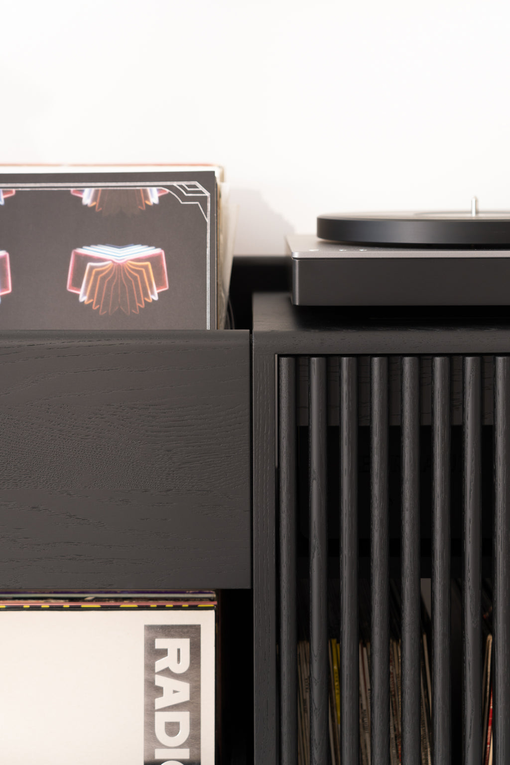 Vinyl records stored in a sleek black wooden cabinet next to a turntable.