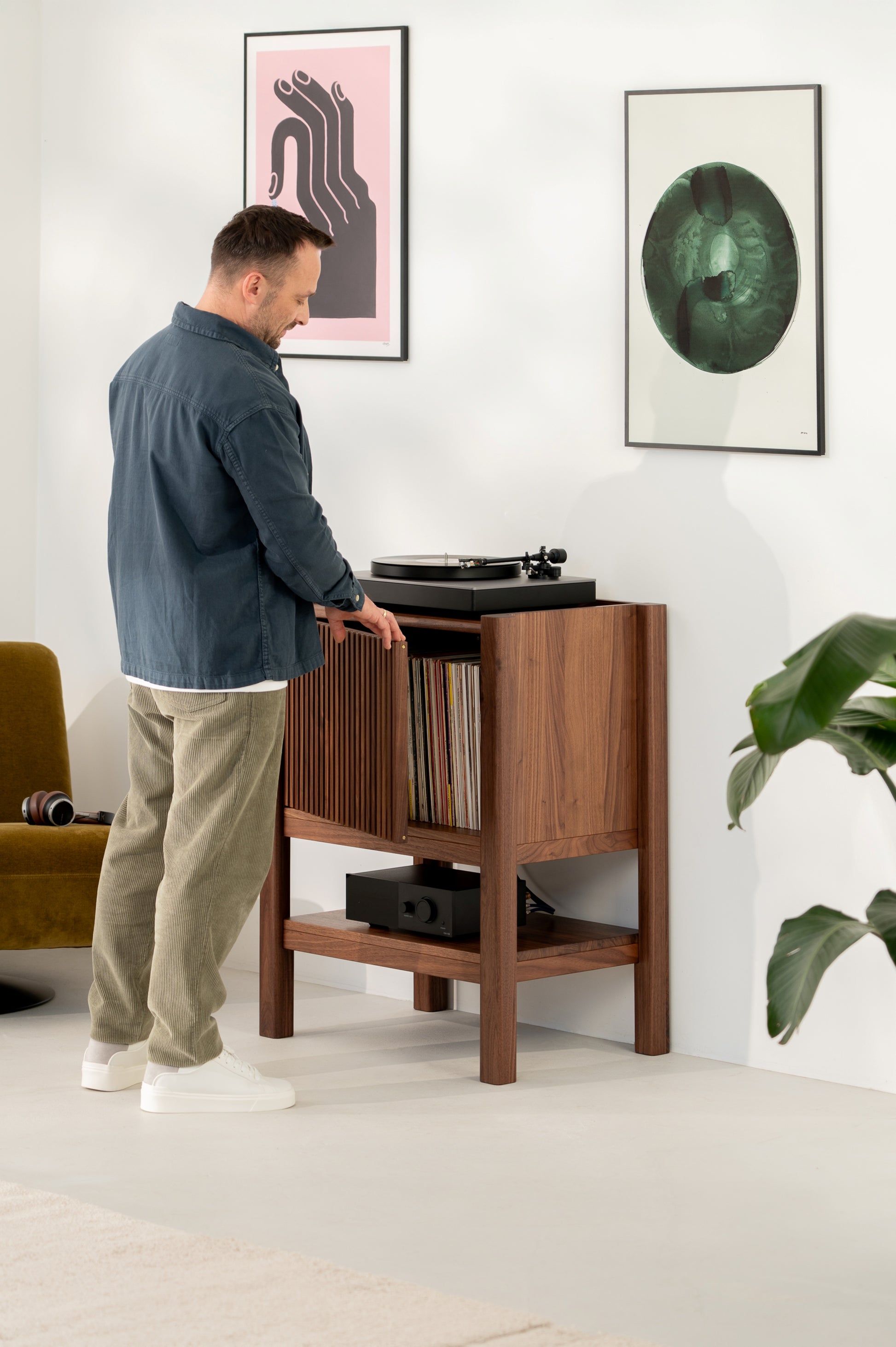 Man selecting a vinyl record from a wooden cabinet next to a turntable, with framed art on the wall.