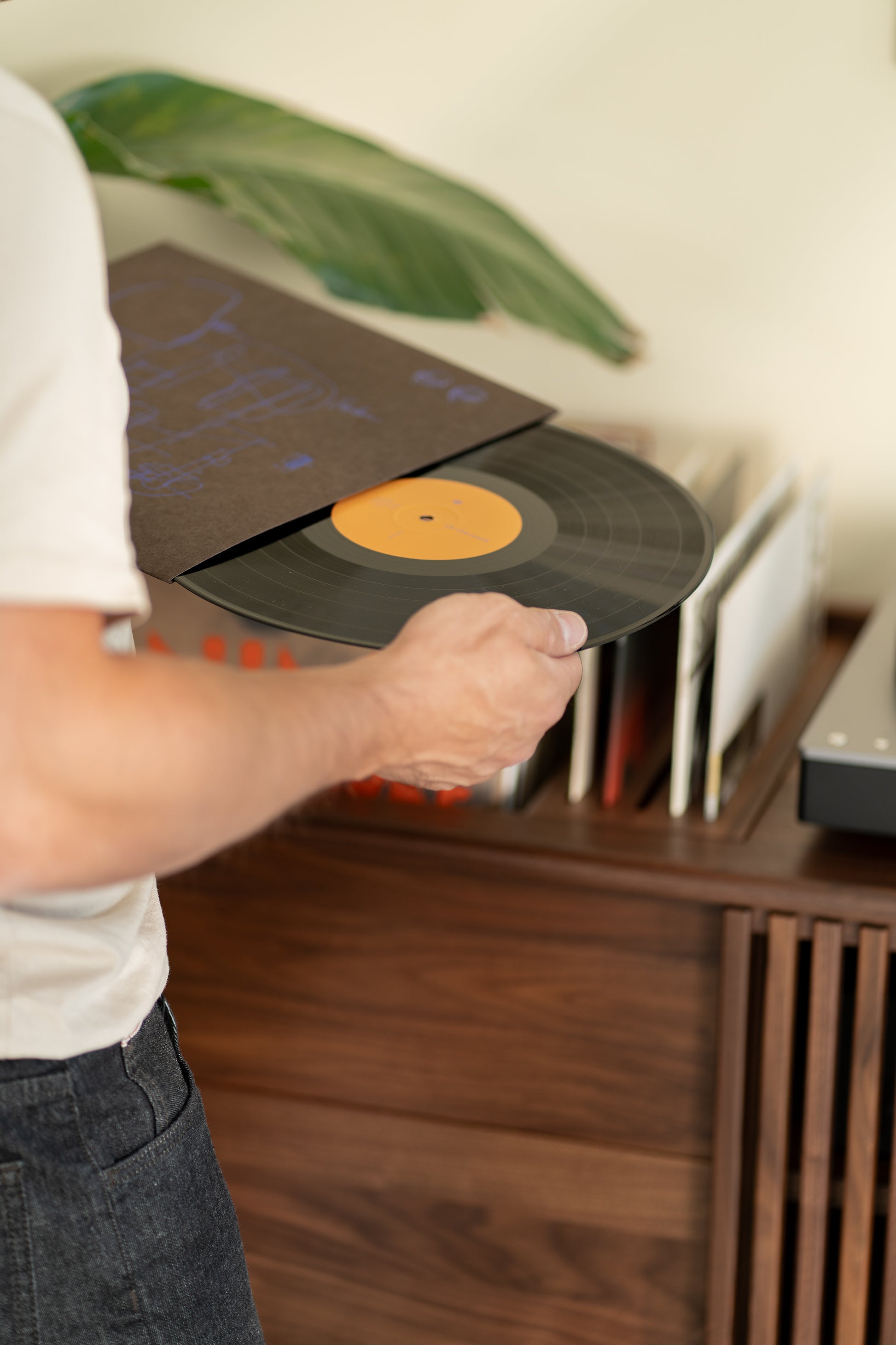 Person holding a vinyl record from its sleeve near a wooden cabinet.