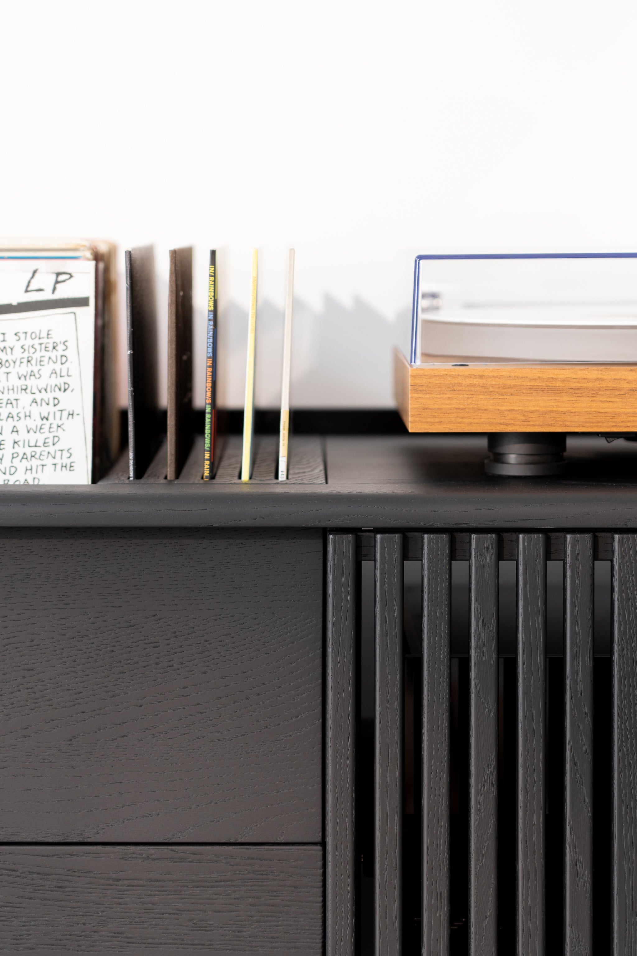 Vinyl records stand next to a modern turntable on a dark wooden shelf.
