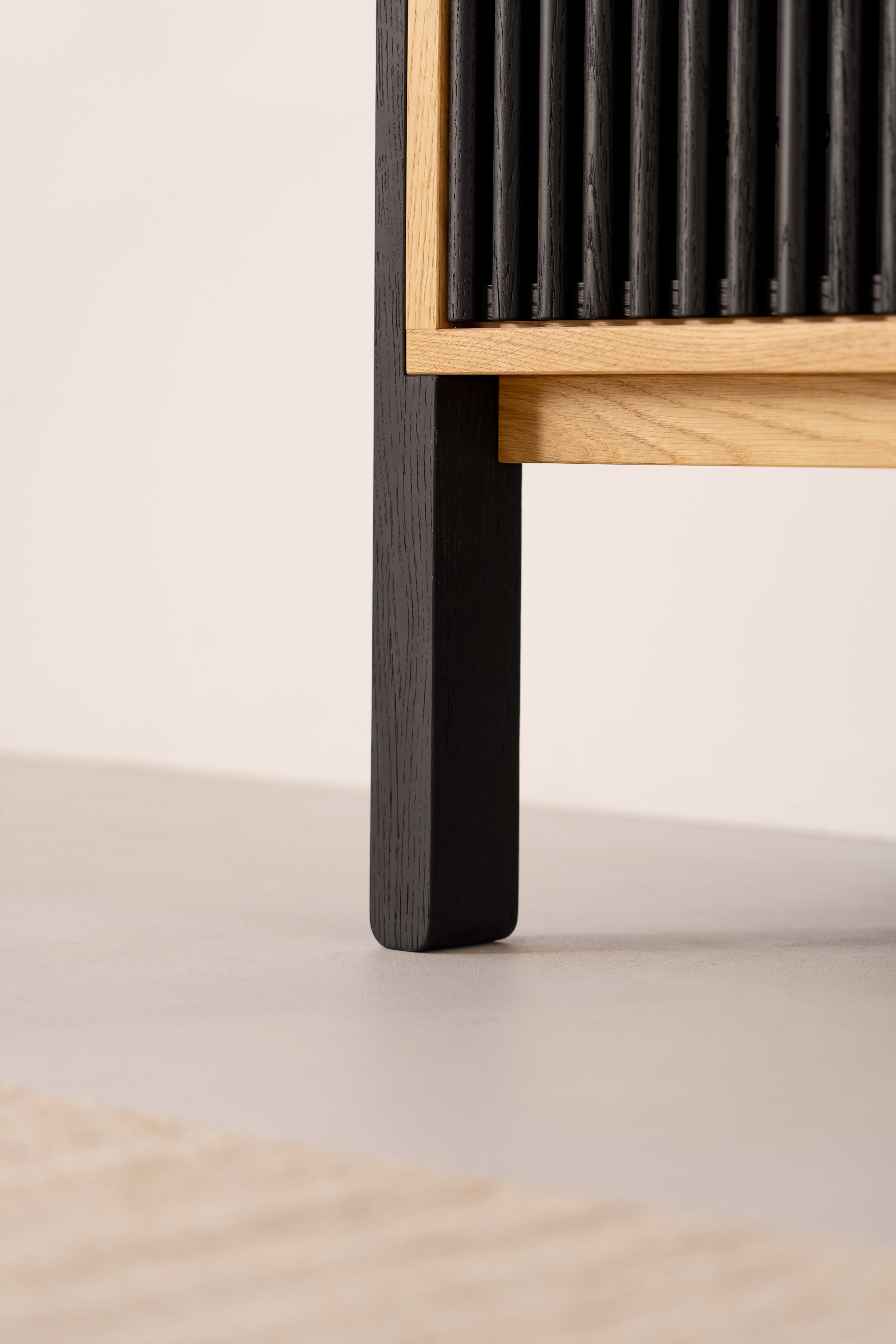 Close-up of a black wooden chair leg with a slatted design and light wood accents.