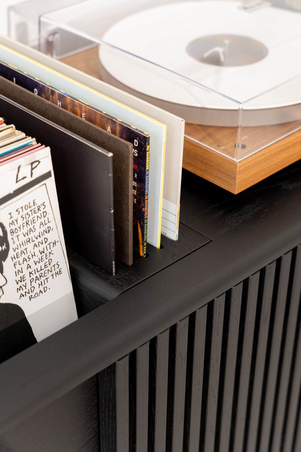 Close-up of a black oak cabinet. Inside are vinyl records, next to it stands a turntable.