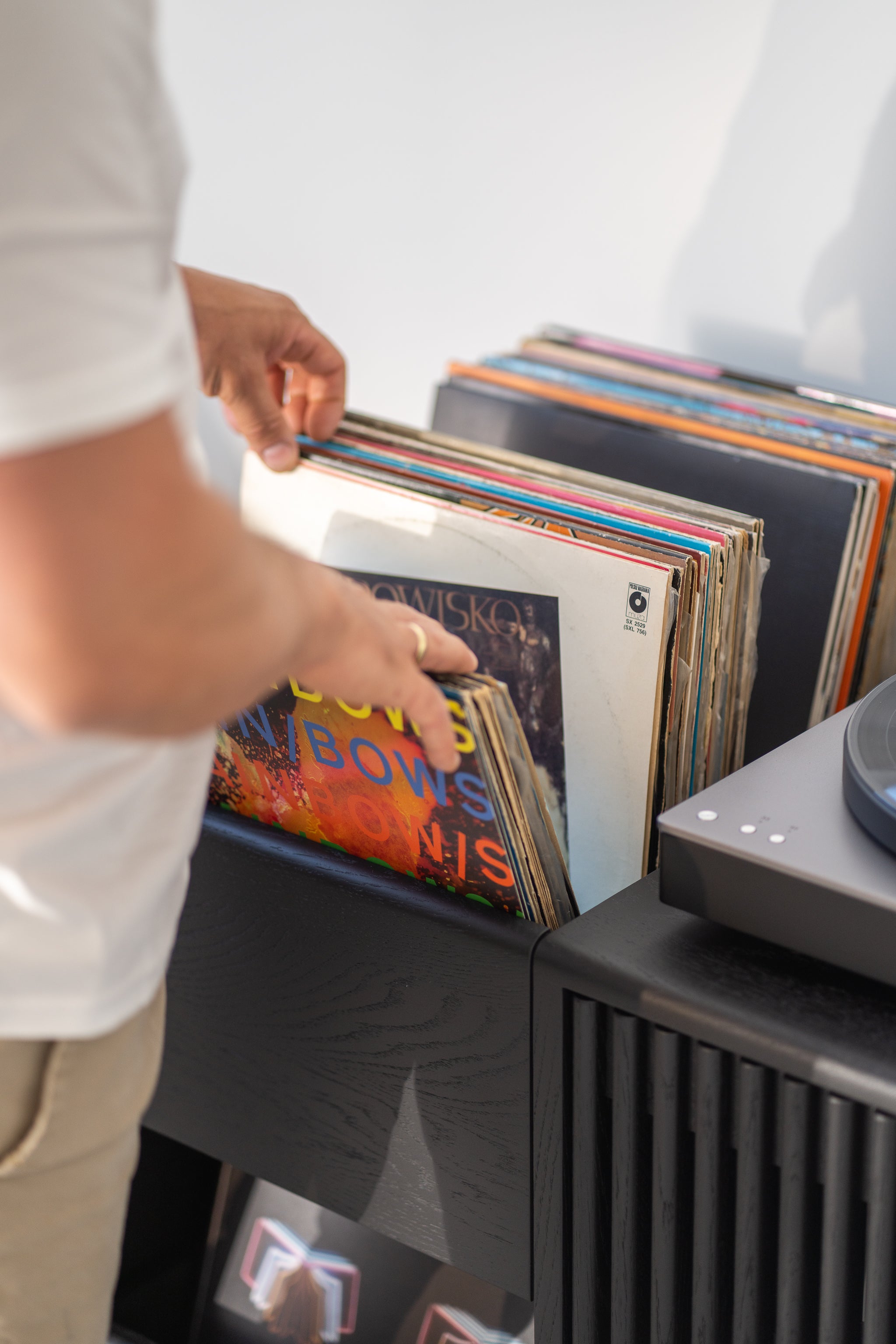 Person flipping through vinyl records on a shelf next to a turntable.