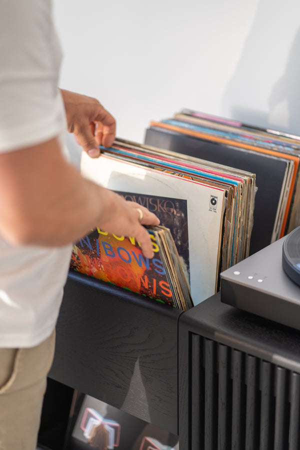 Person flipping through vinyl records on a shelf next to a turntable.
