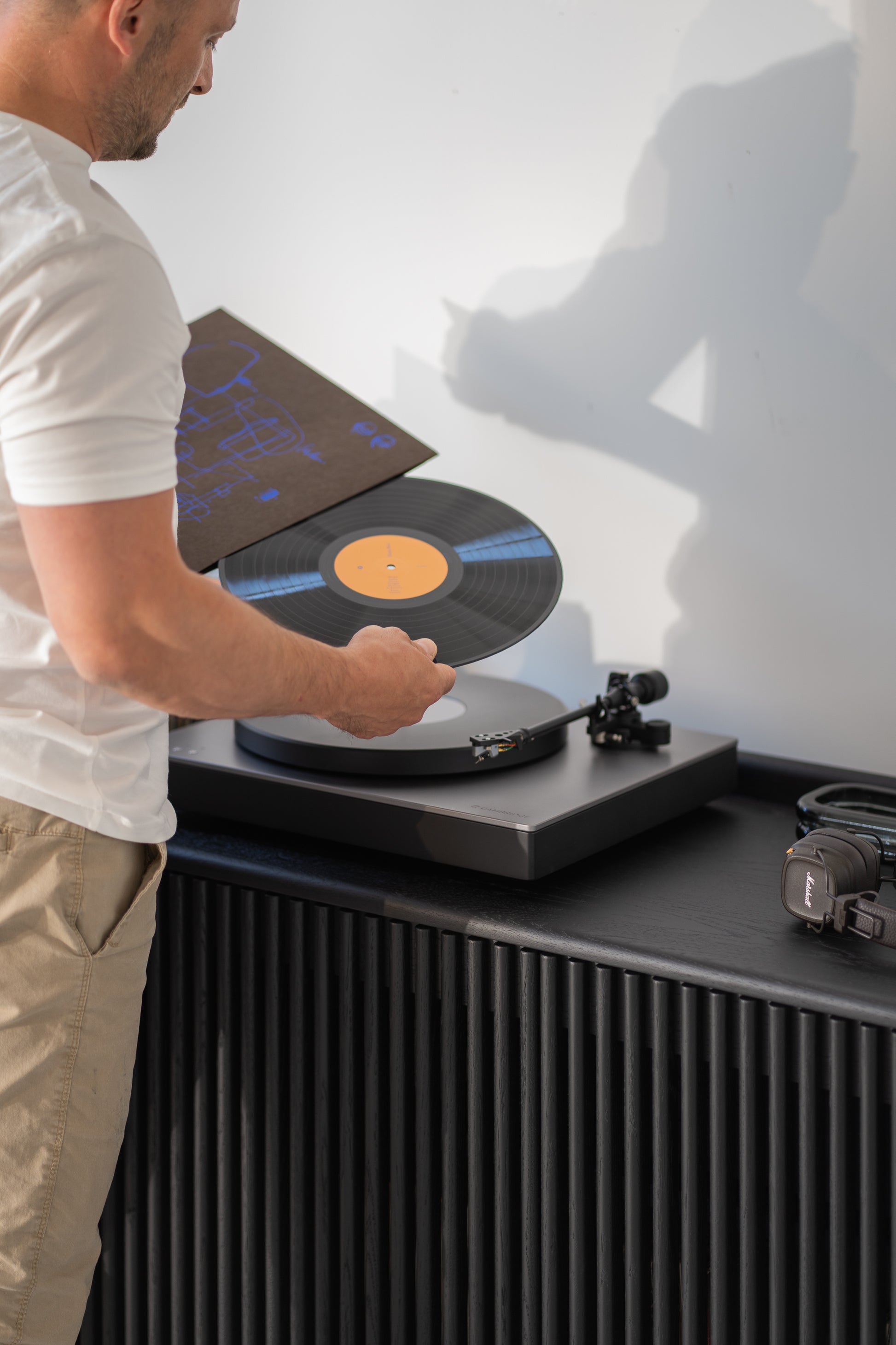 Person placing a vinyl record on a turntable, with headphones on a nearby table.