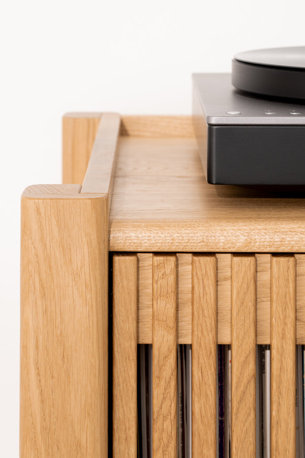 Wooden cabinet corner with vinyl records and a black turntable on top.