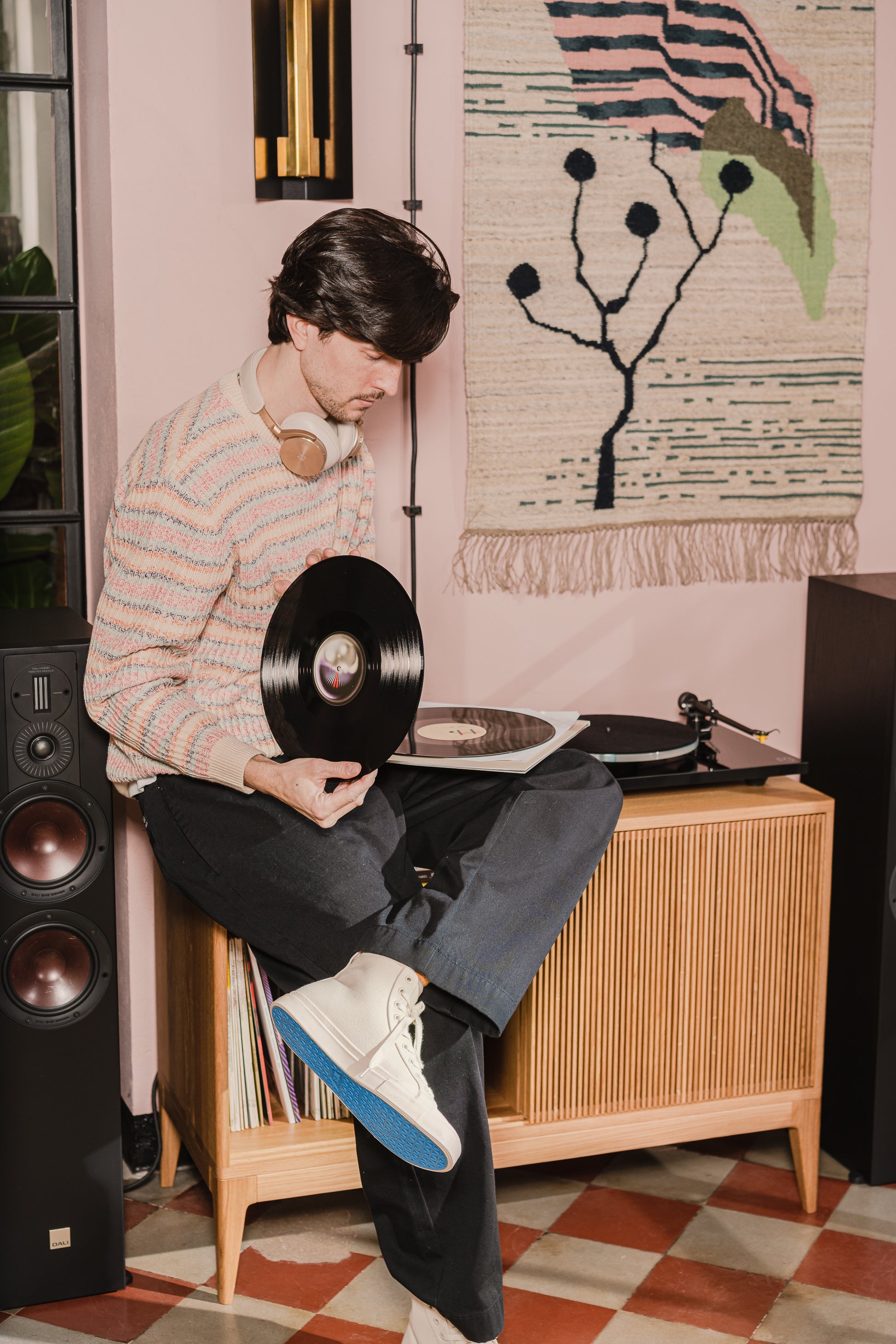 Person holding a vinyl record near a turntable in a cozy room with modern decor.