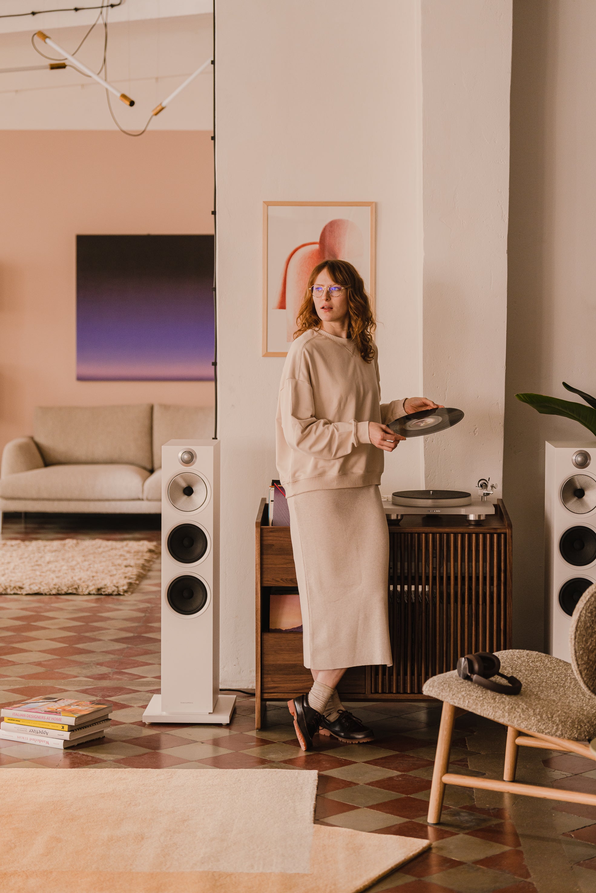 Person holding a vinyl record near a turntable, with modern speakers and cozy living room decor.
