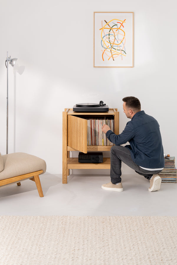 Man browsing vinyl records in a modern living room with a turntable and abstract wall art.