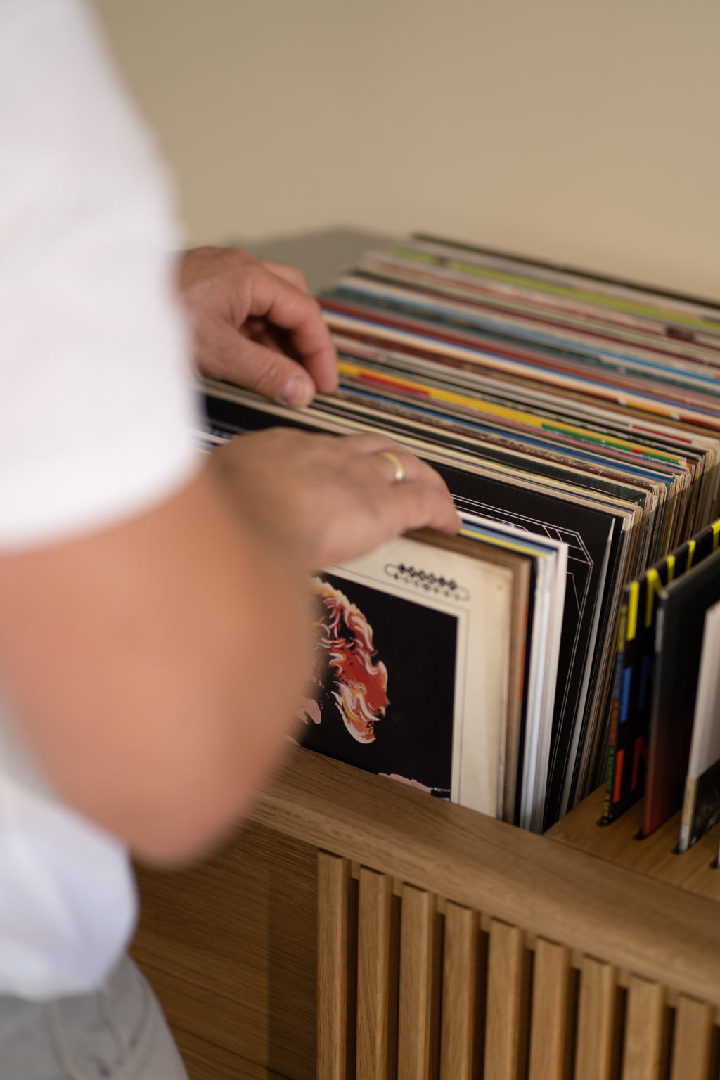 Person flipping through vinyl records in a wooden cabinet.