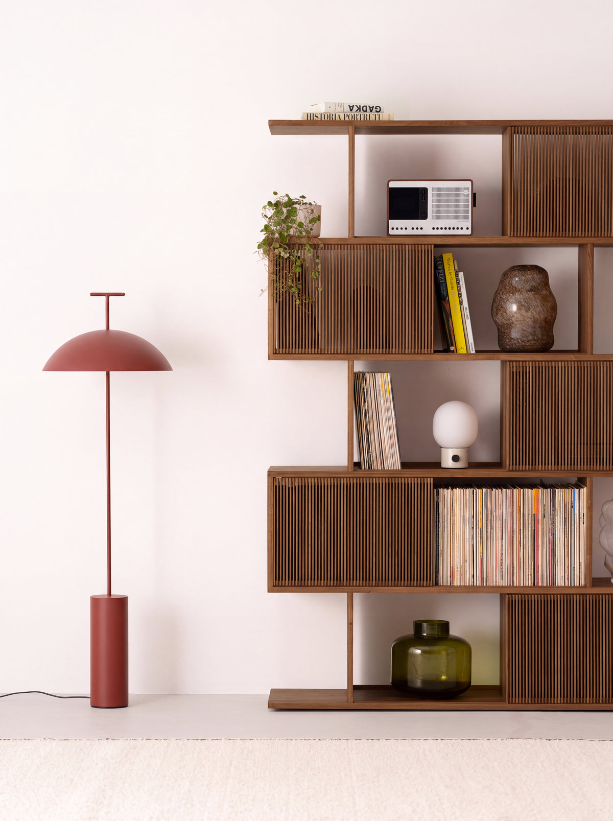 Angled view of the MOLL solid walnut bookcase beside a red floor lamp, with records and decor on the shelves