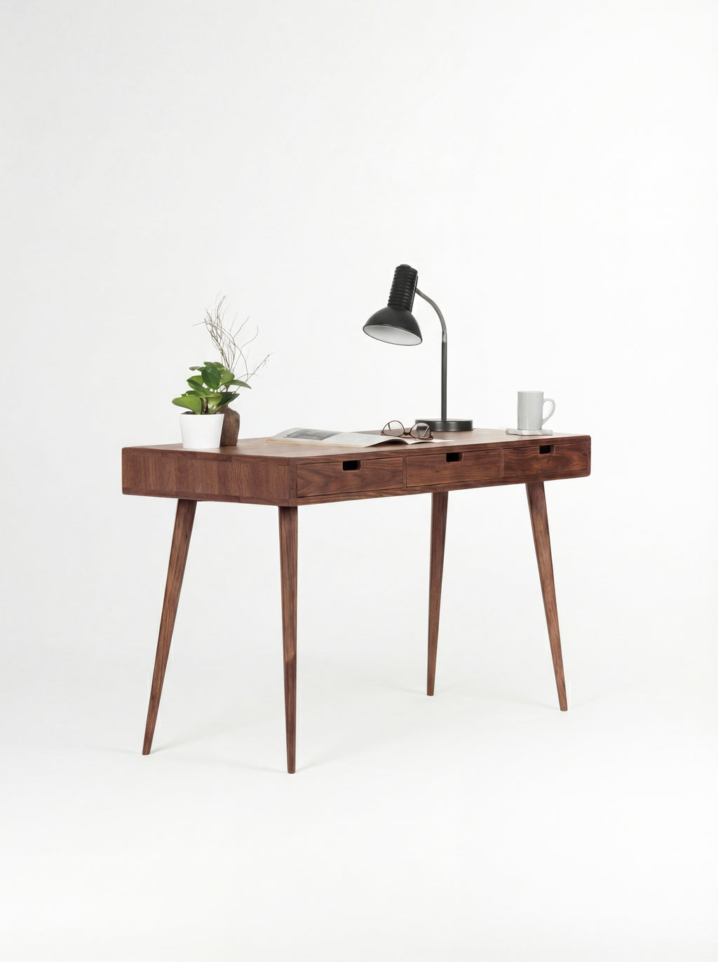 HEIM 140 desk in solid walnut at an angle, with an open magazine, glasses and a mug on top