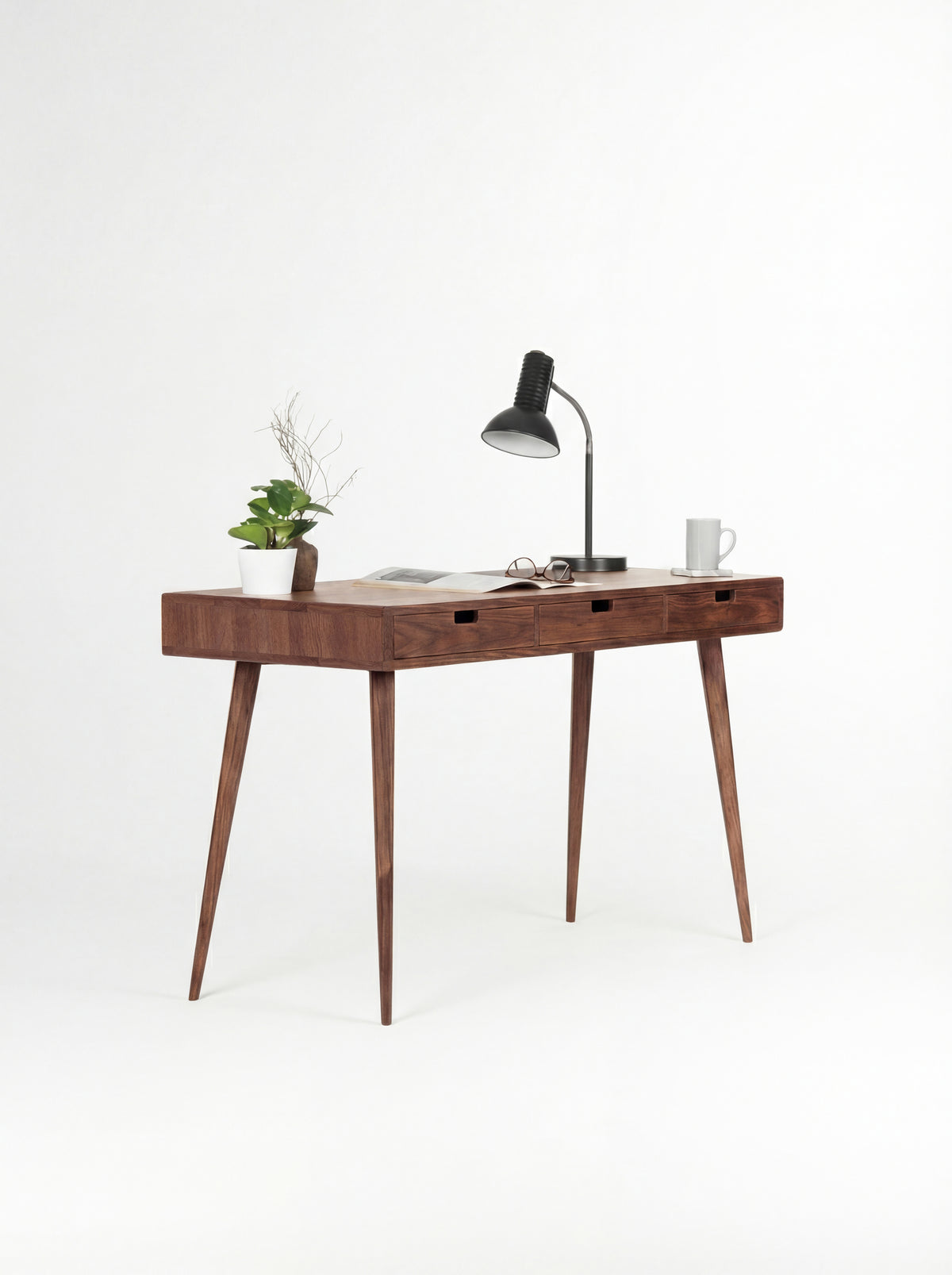 HEIM 140 desk in solid walnut at an angle, with an open magazine, glasses and a mug on top