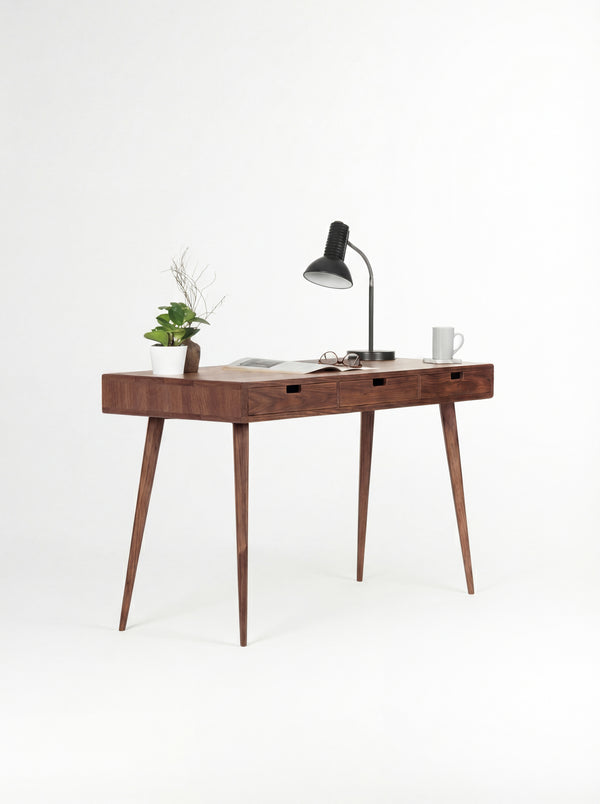 HEIM 140 desk in solid walnut at an angle, with an open magazine, glasses and a mug on top
