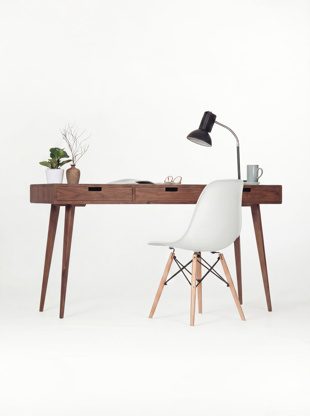 HEIM 140 desk in solid walnut, front view with a white shell chair, black lamp and open magazine