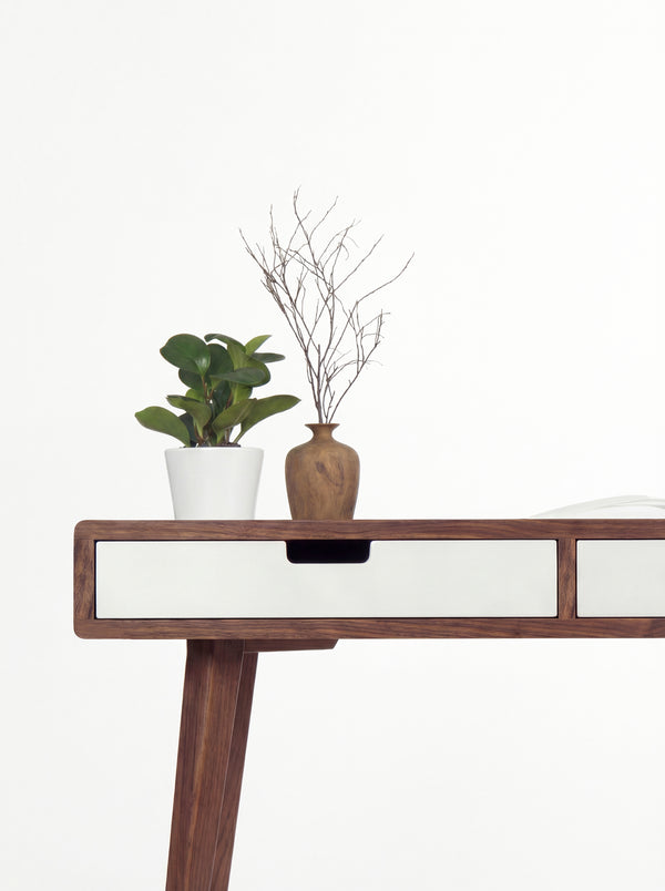 Close-up of a white drawer front and cut-out grip on the HEIM 140 in solid walnut, with a wooden vase above
