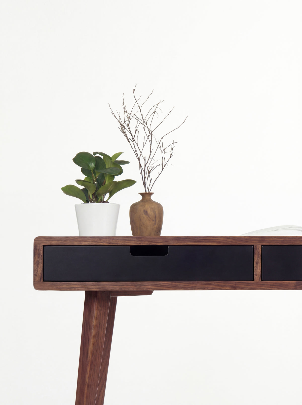 HEIM 140 in solid walnut, close-up of a black drawer front with a cut-out grip and a walnut leg below