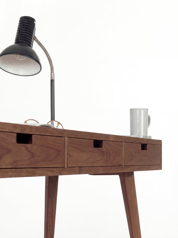 HEIM 140 in solid walnut, close-up of three drawer fronts with cut-out grips beneath a black lamp and mug