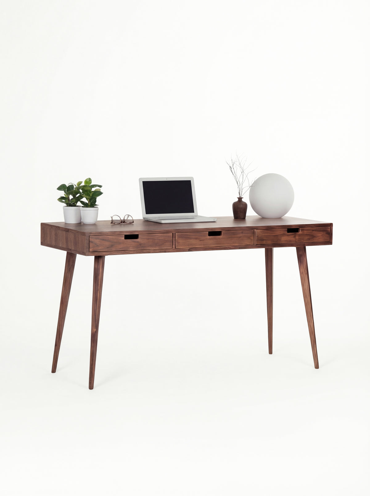HEIM 140 solid walnut desk at a three-quarter angle with a laptop, plants and a globe lamp