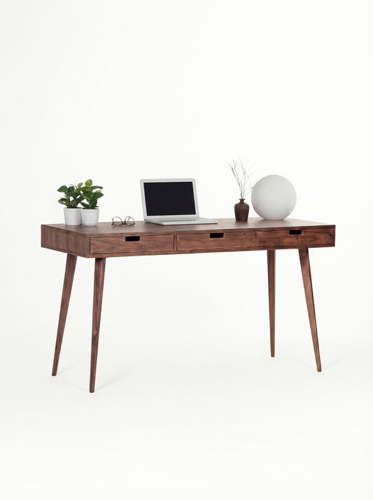 HEIM 140 solid walnut desk at a three-quarter angle with a laptop, plants and a globe lamp