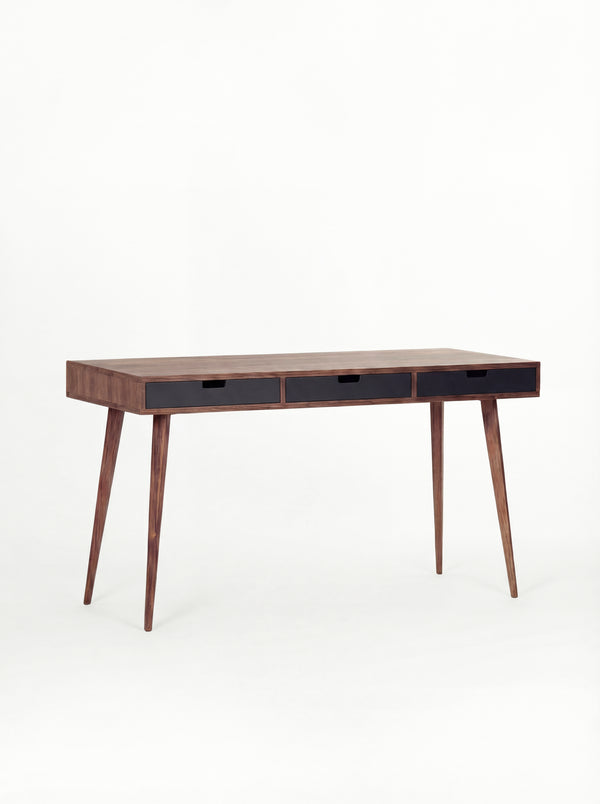 Empty HEIM 140 desk in solid walnut with three black drawer fronts, angled against a white background