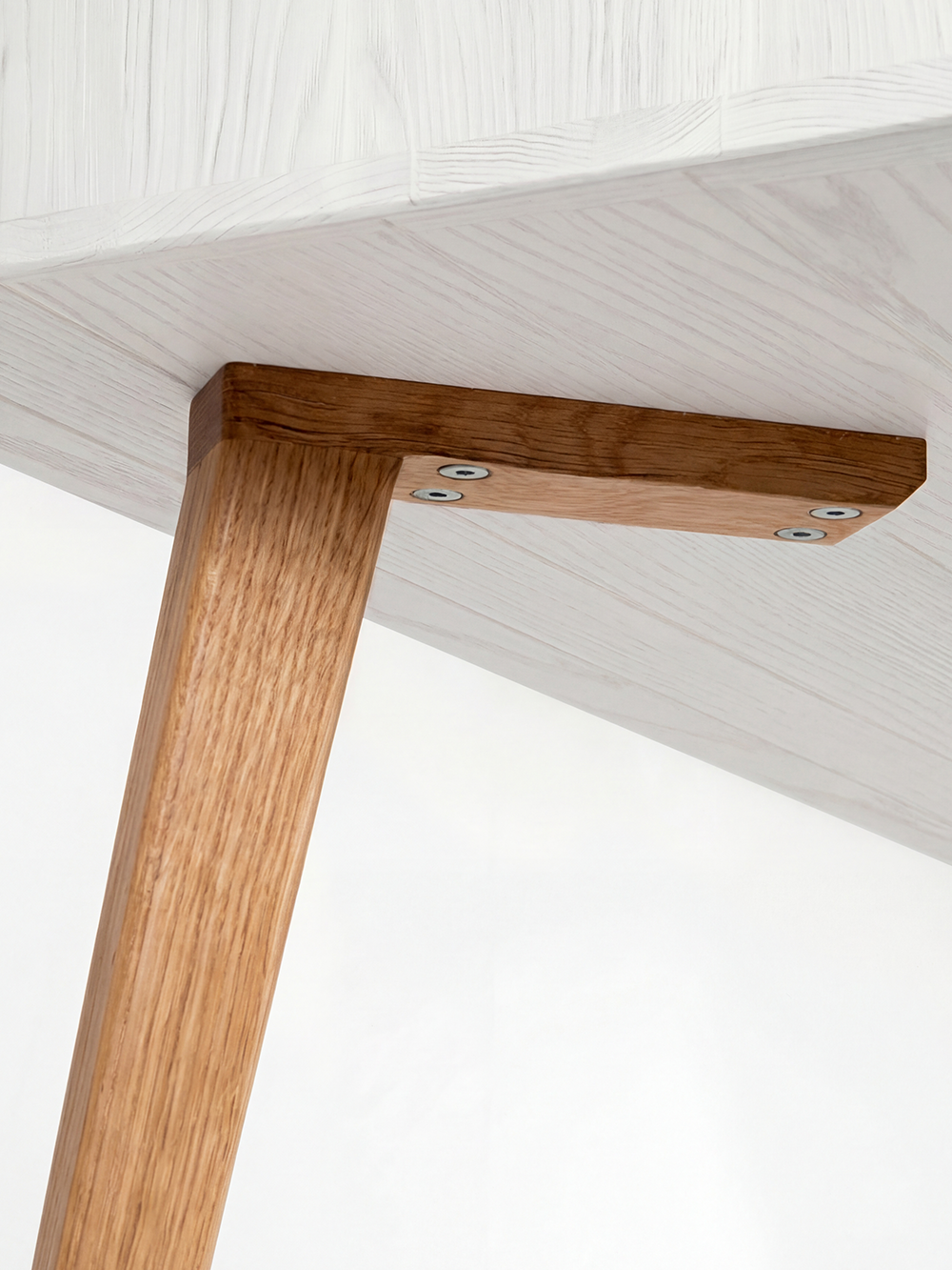 Underside of the HEIM 140 desk in solid oak, showing the leg mounting block and grain beneath white lacquer