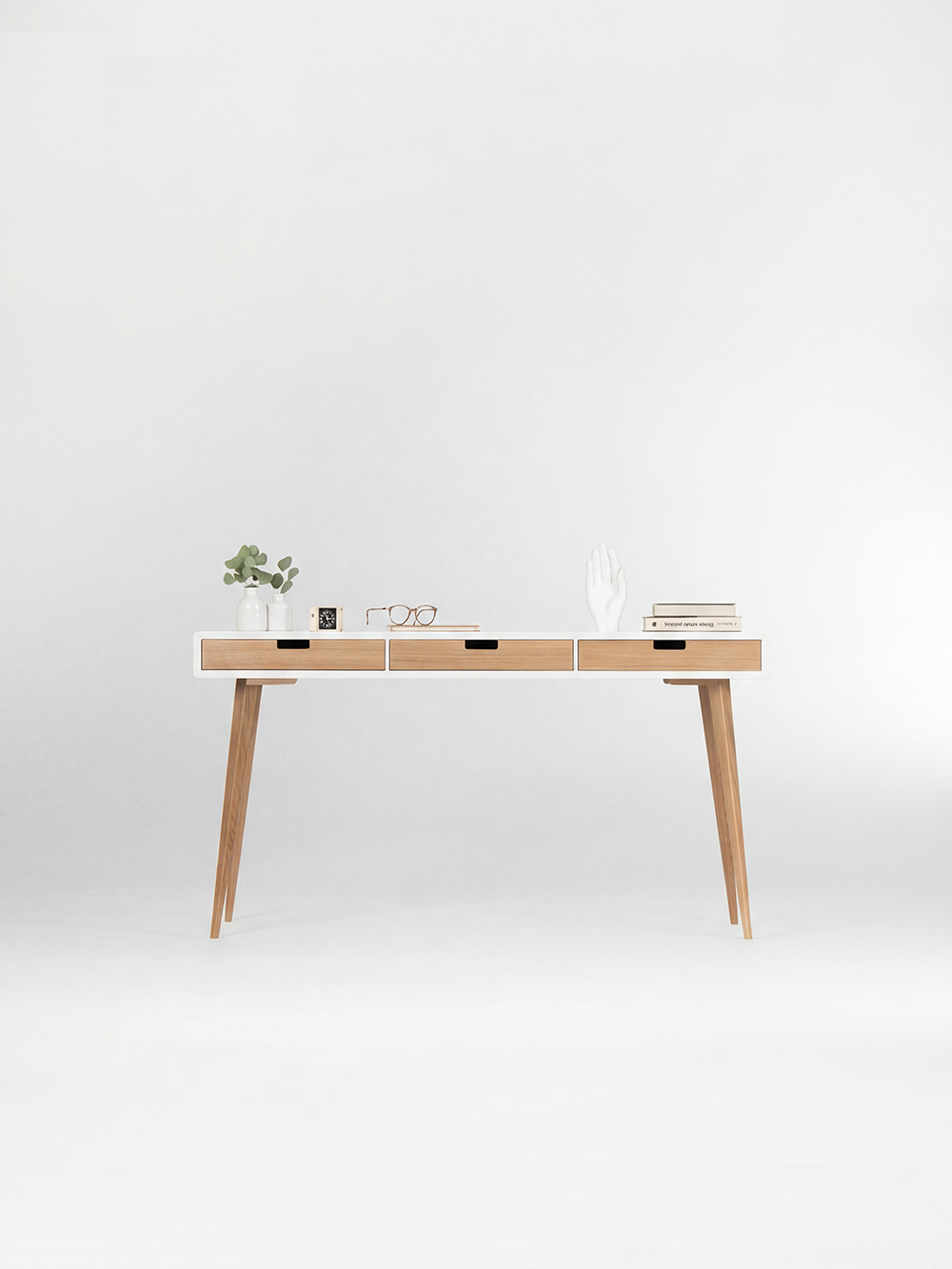 Front view of the HEIM 140 white desk in solid oak, with three natural oak drawer fronts and decor on top