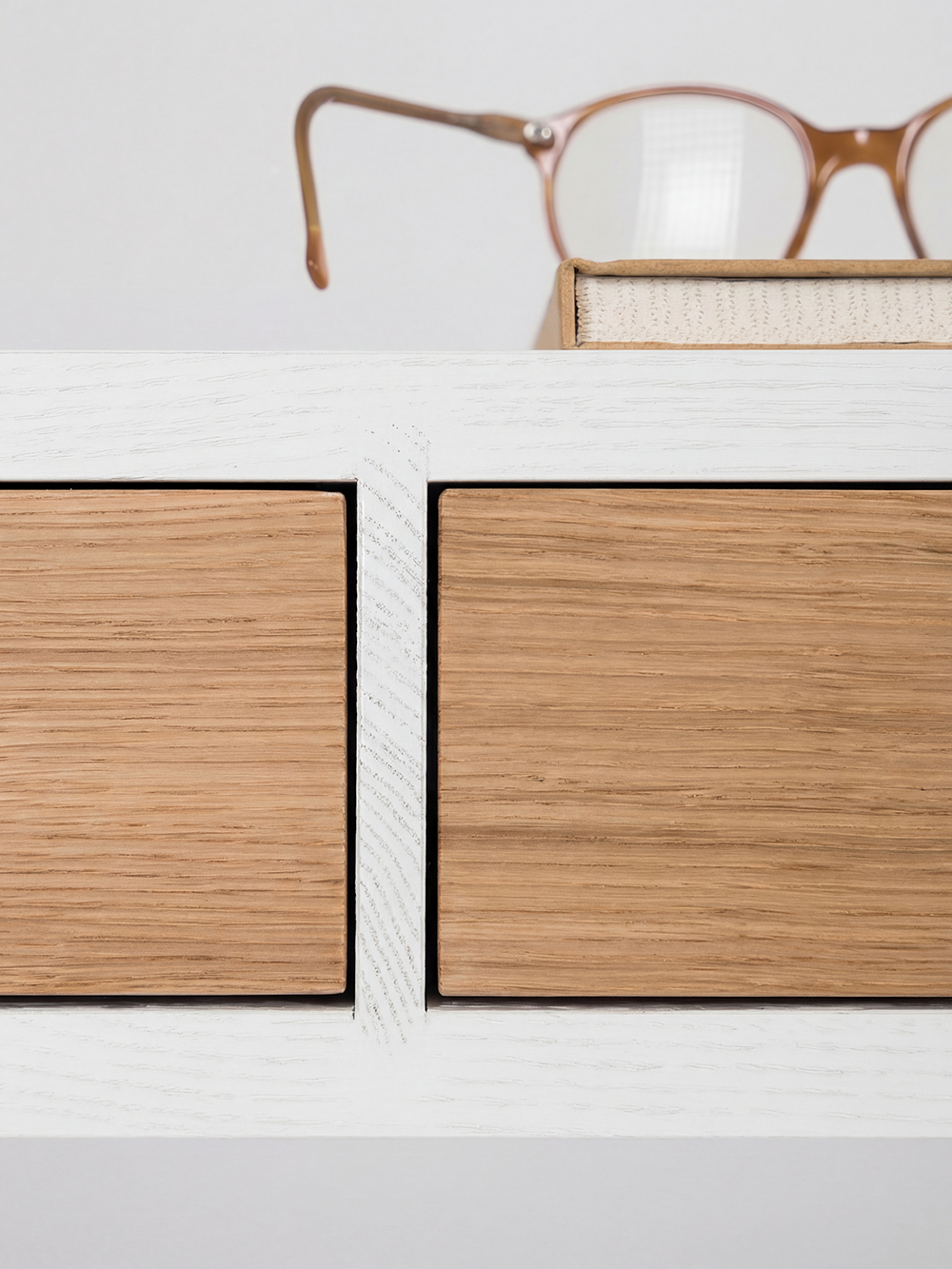 HEIM 140 desk in solid oak, close-up of two oak fronts and a white divider, with glasses resting on a notebook