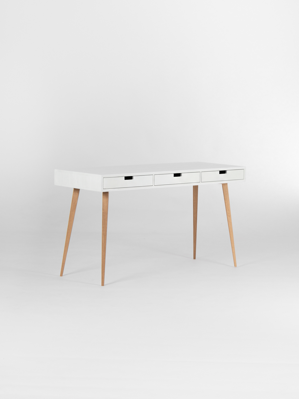 HEIM 140 desk in solid oak, shown empty at an angle with a white body, three white drawer fronts and natural oak legs