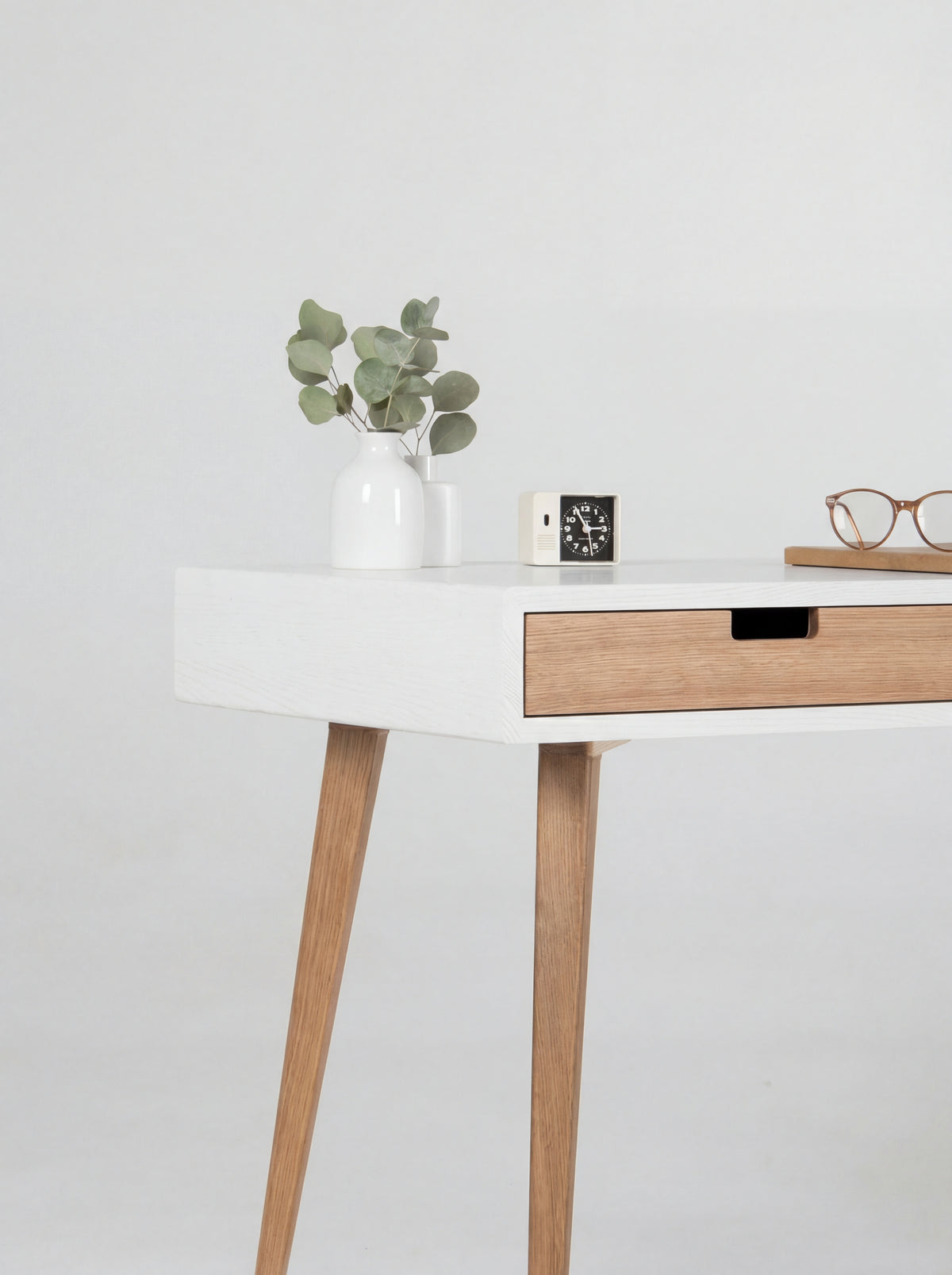 Close-up of the HEIM 140 desk in oak wood, showing its white body corner, oak drawer front and cut-out grip