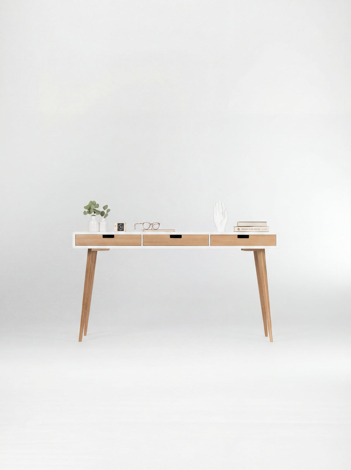 Front view of the HEIM 140 desk in oak wood, with a white body, three natural oak drawer fronts and books on top