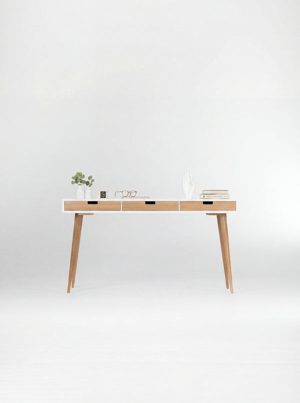 Front view of the HEIM 140 desk in oak wood, with a white body, three natural oak drawer fronts and books on top