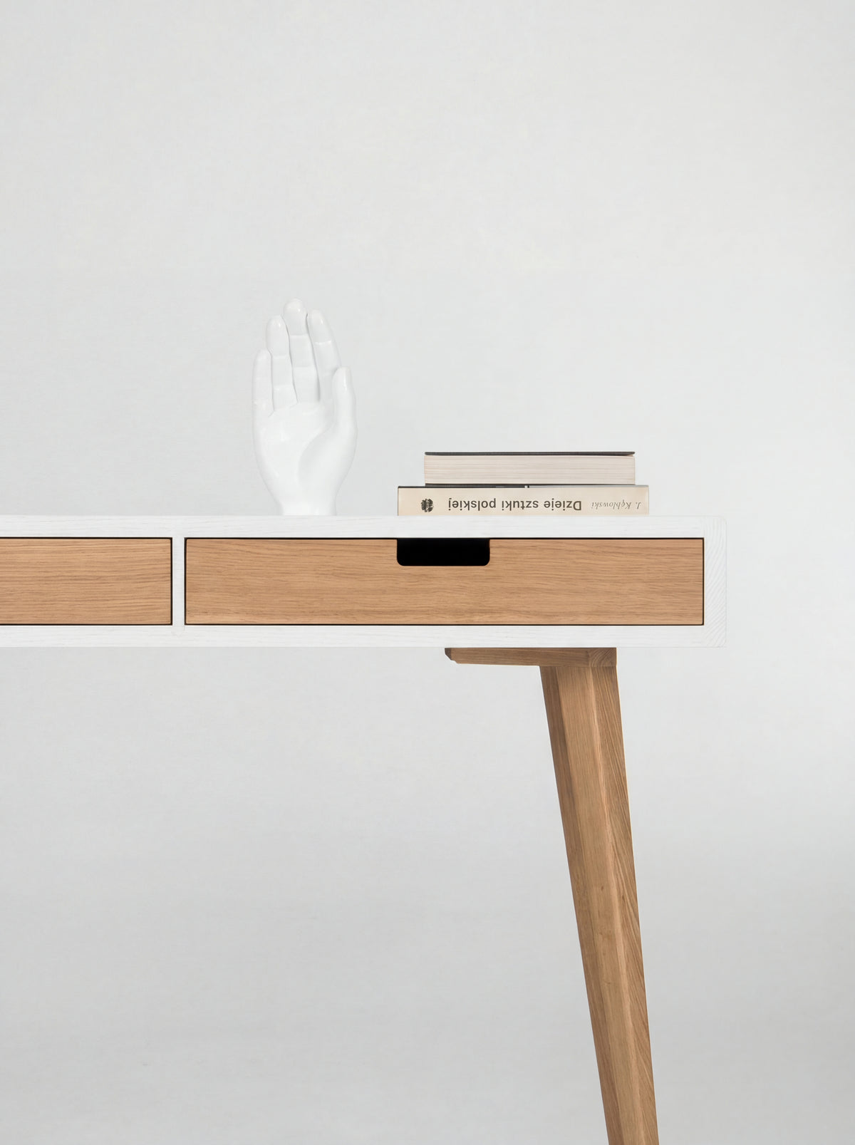Right end of the HEIM 140 desk in oak wood, showing an angled leg, a white hand sculpture and books