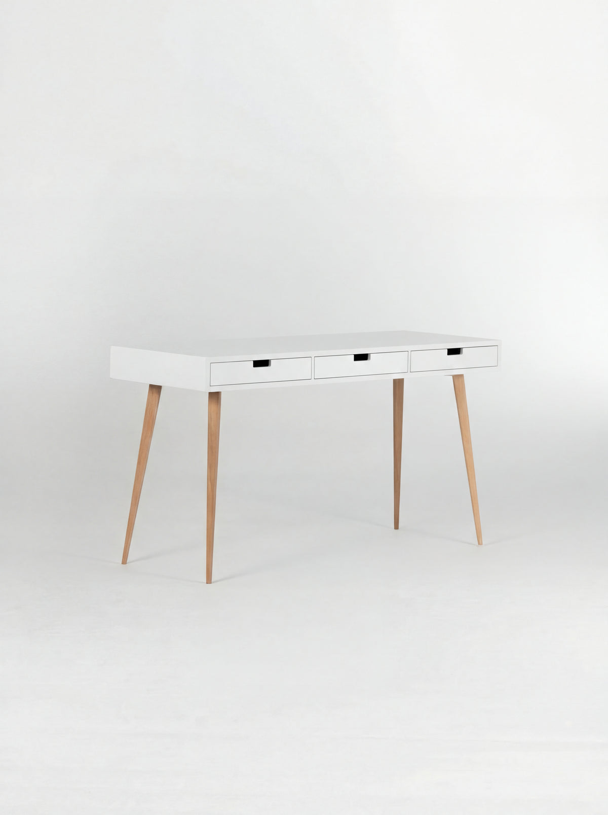 Angled view of the empty HEIM 140 desk in oak wood, with a white body, three white drawer fronts and oak legs