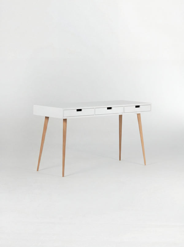 Angled view of the empty HEIM 140 desk in oak wood, with a white body, three white drawer fronts and oak legs