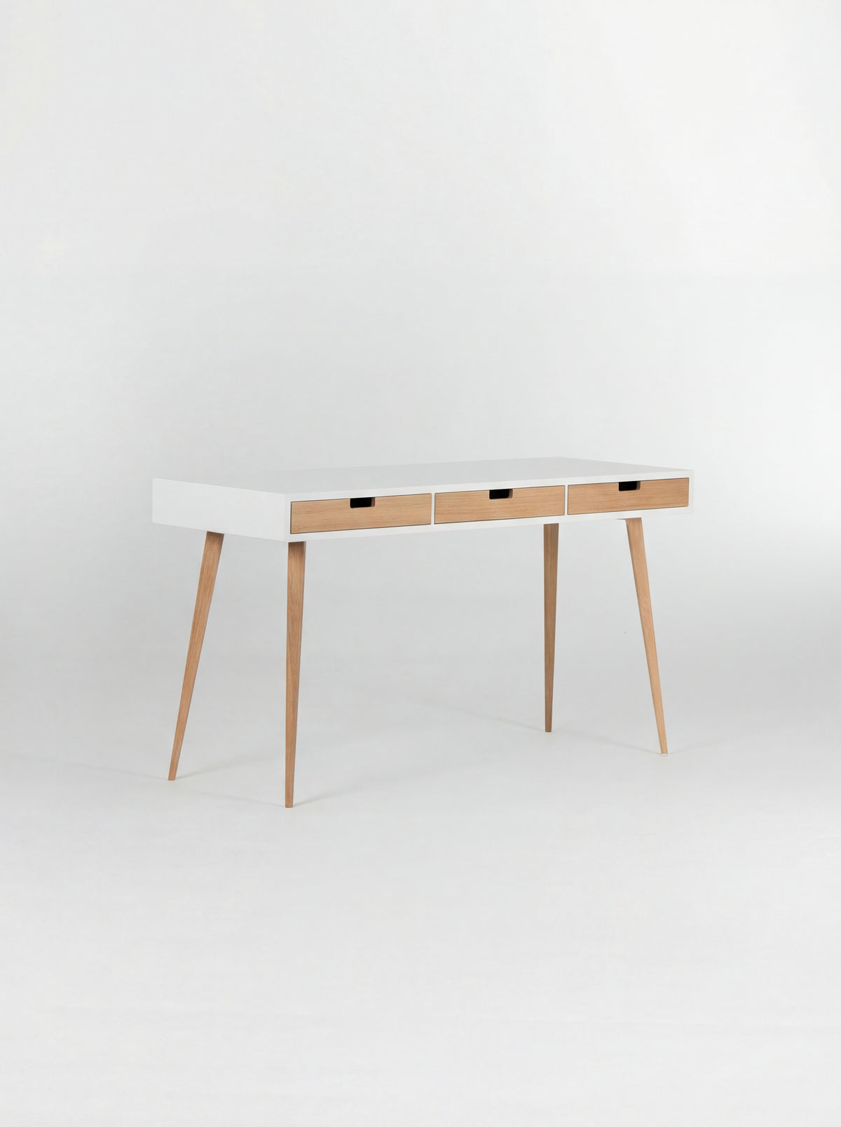 HEIM 140 desk in oak wood, empty and angled to show its white body, three natural oak drawer fronts and oak legs