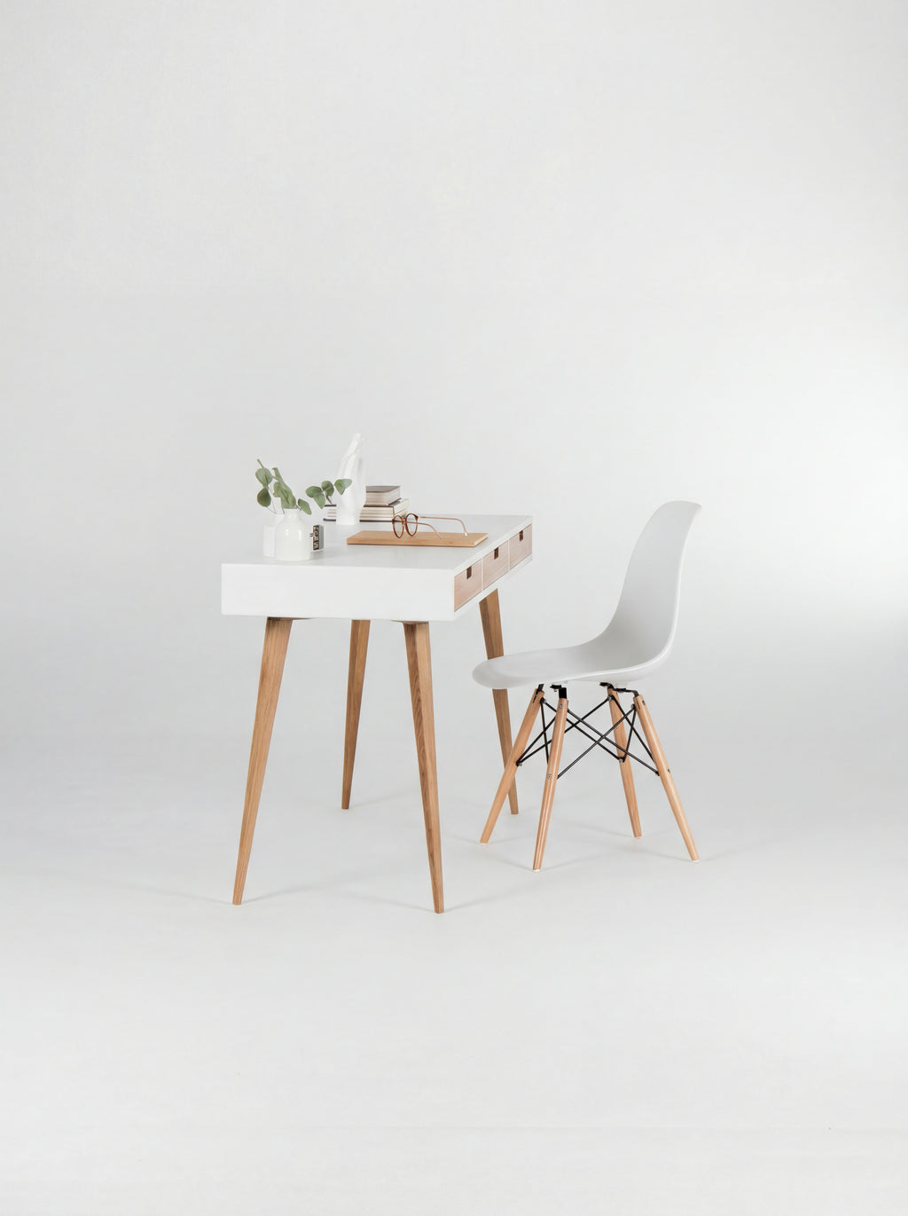 HEIM 140 white writing desk in oak wood, viewed from the short end with a shell chair, eucalyptus and books