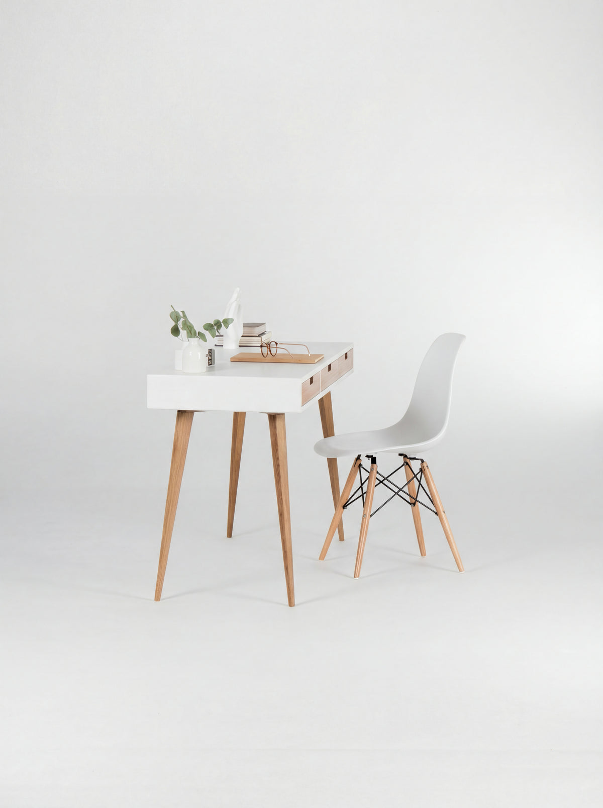 HEIM 140 white writing desk in oak wood, viewed from the short end with a shell chair, eucalyptus and books
