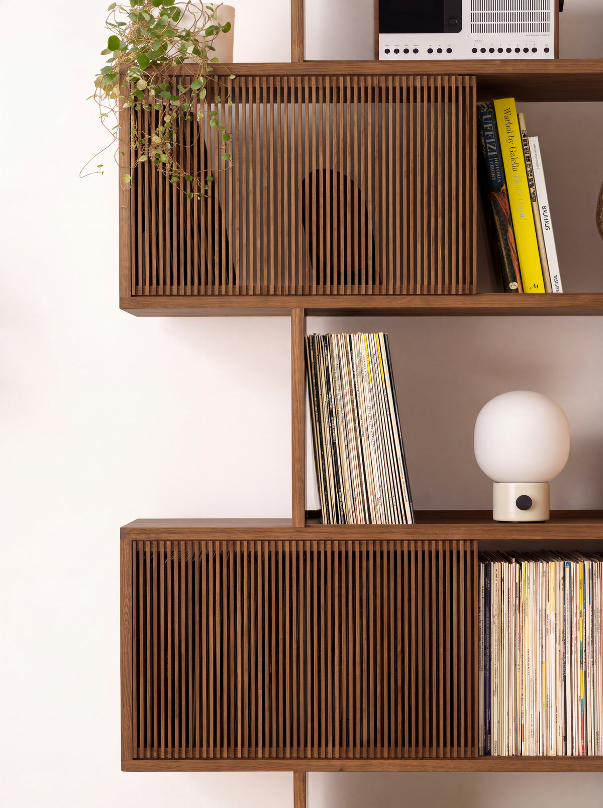 Middle shelves of MOLL in solid walnut, with slatted fronts, records, books, a small lamp and a trailing plant