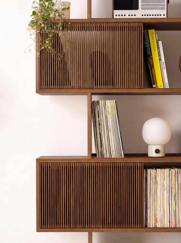 Middle shelves of MOLL in solid walnut, with slatted fronts, records, books, a small lamp and a trailing plant