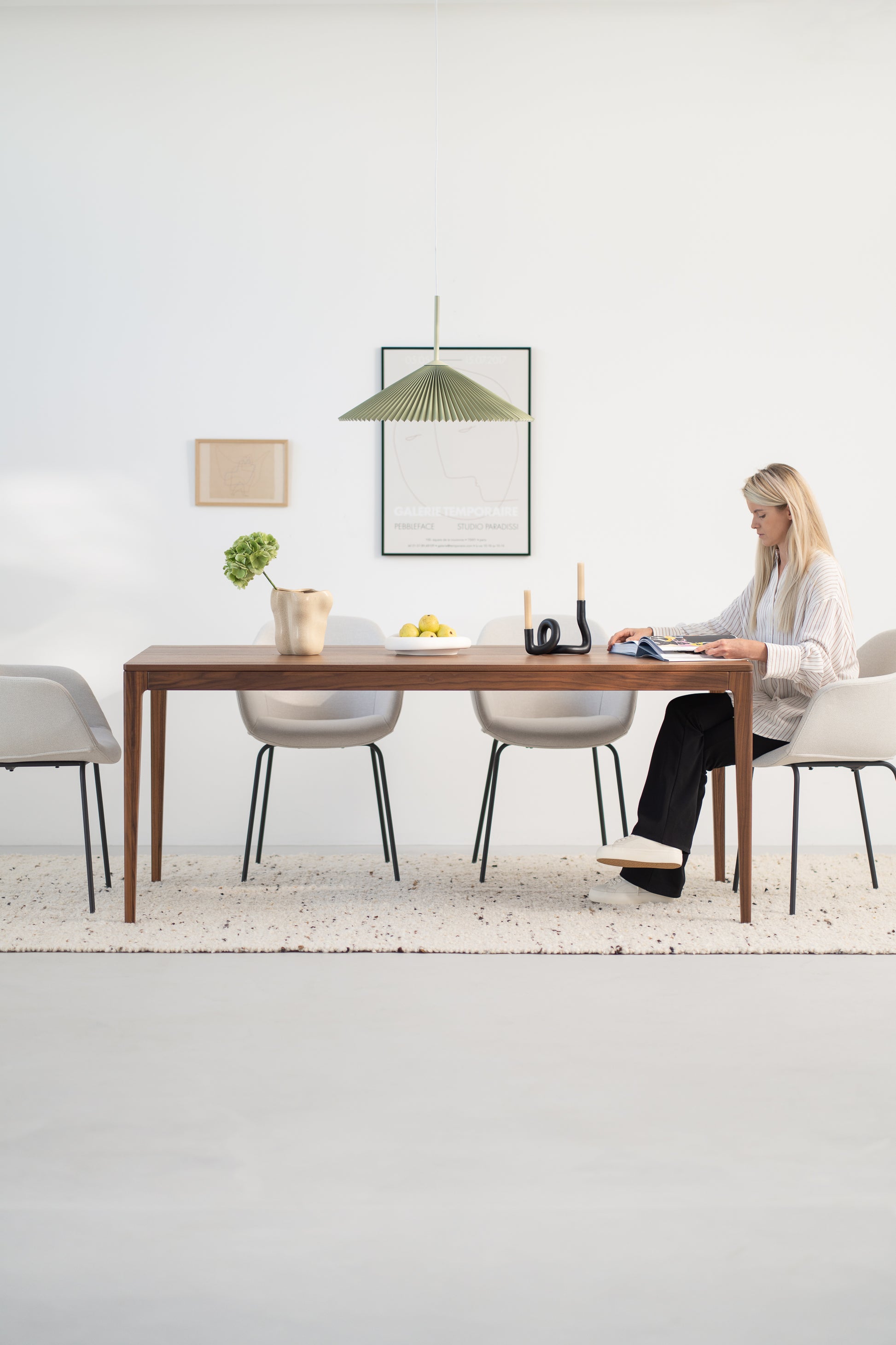 A woman sits at a wooden table reading in a minimalist dining room with neutral tones.