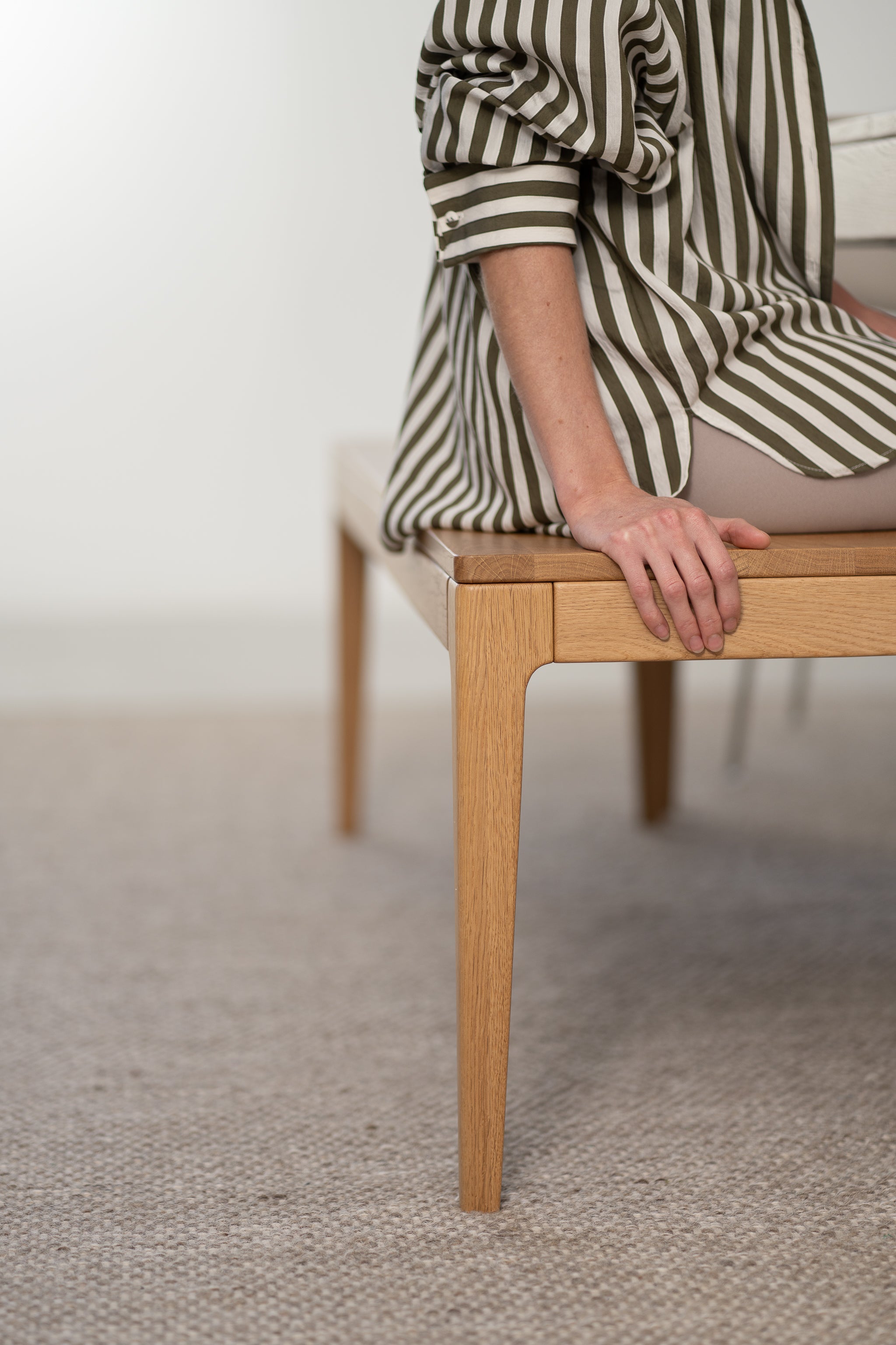 Person in a striped shirt sitting on a wooden bench, hand resting beside them.