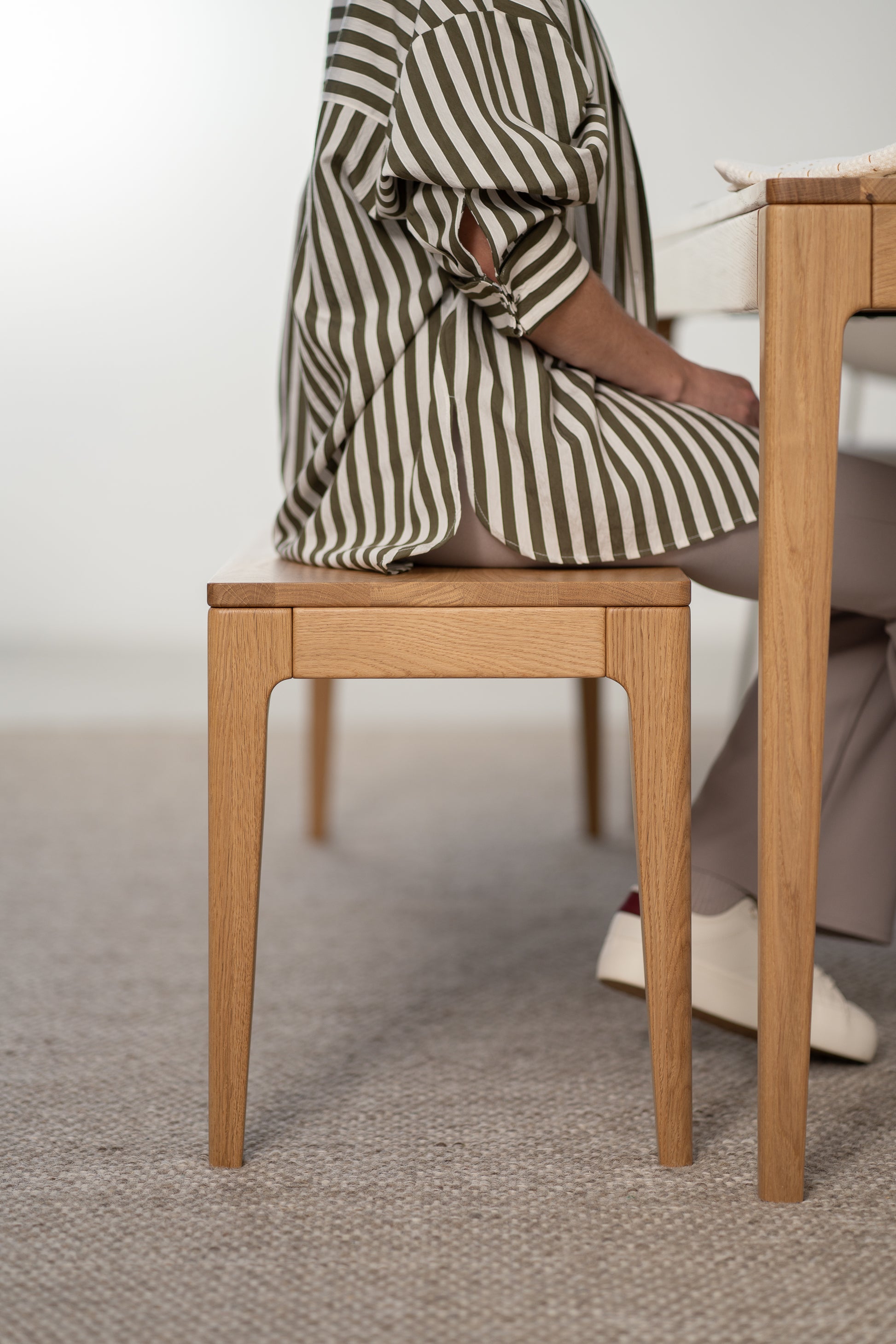 Person in striped shirt sitting on a wooden bench at a table.