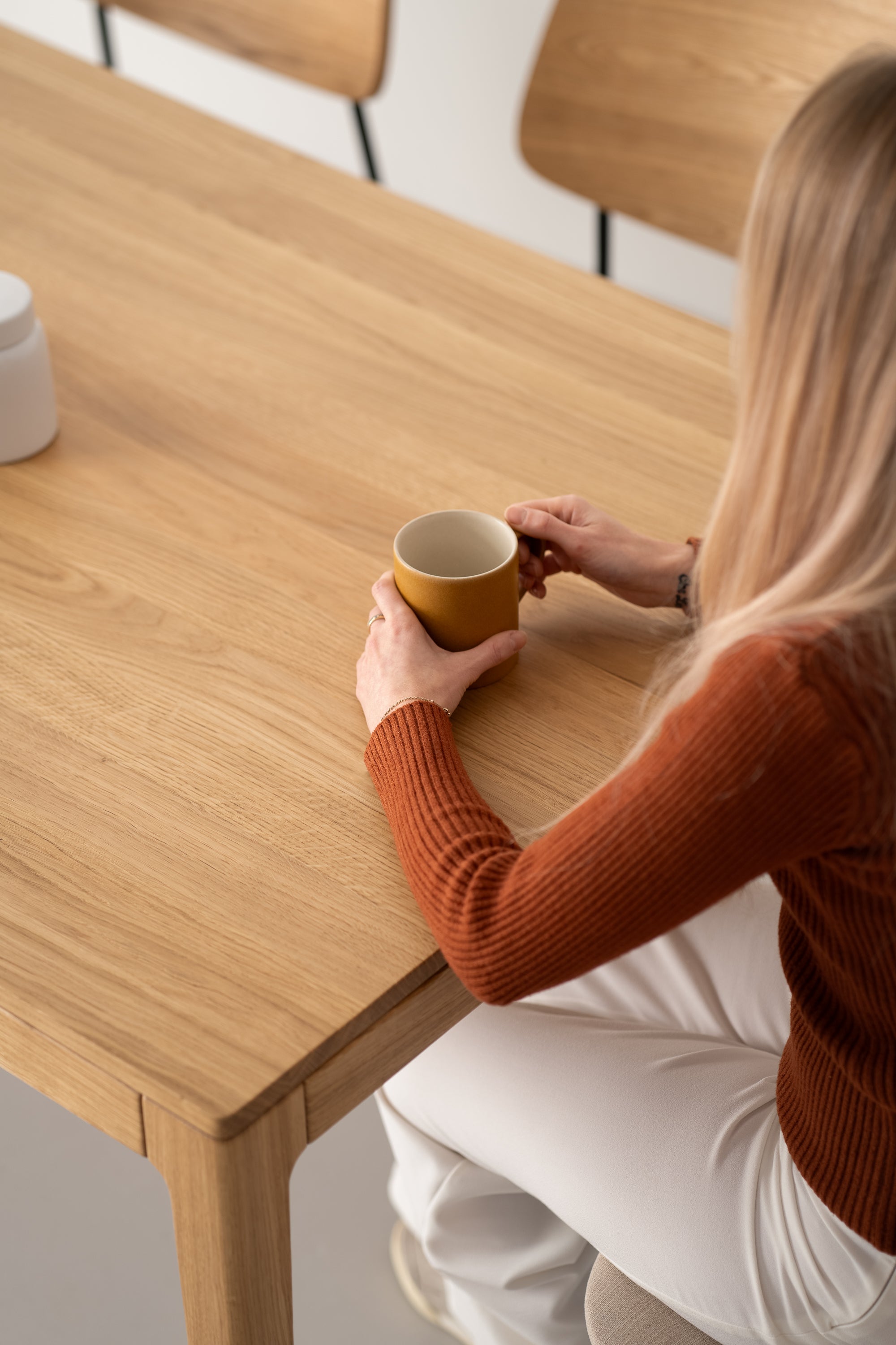 Person holding a yellow mug while sitting at a wooden table.
