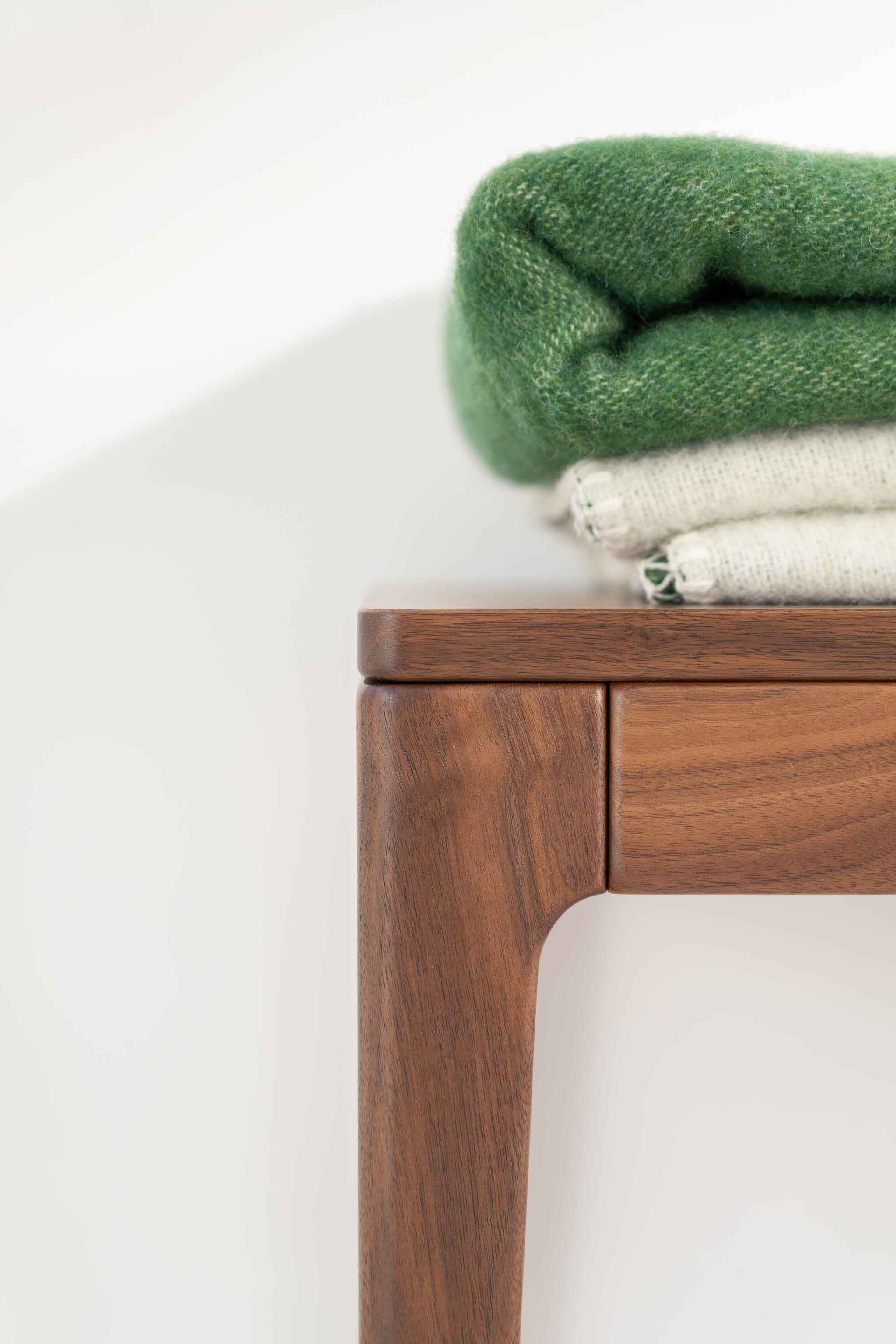 Close-up of a wooden table corner with folded green and white fabric on top.