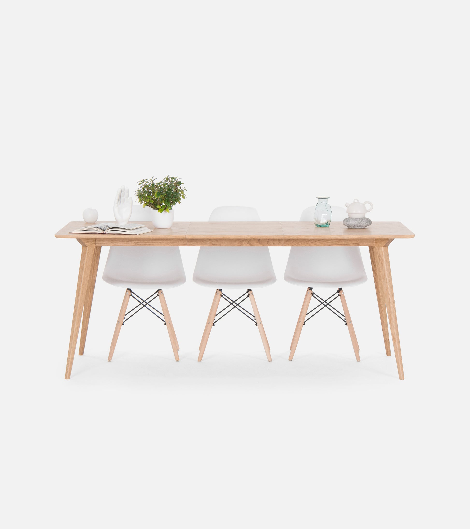 Wood table with three white chairs, decorated with a plant, books, a glass jar, and a teapot on a white background.