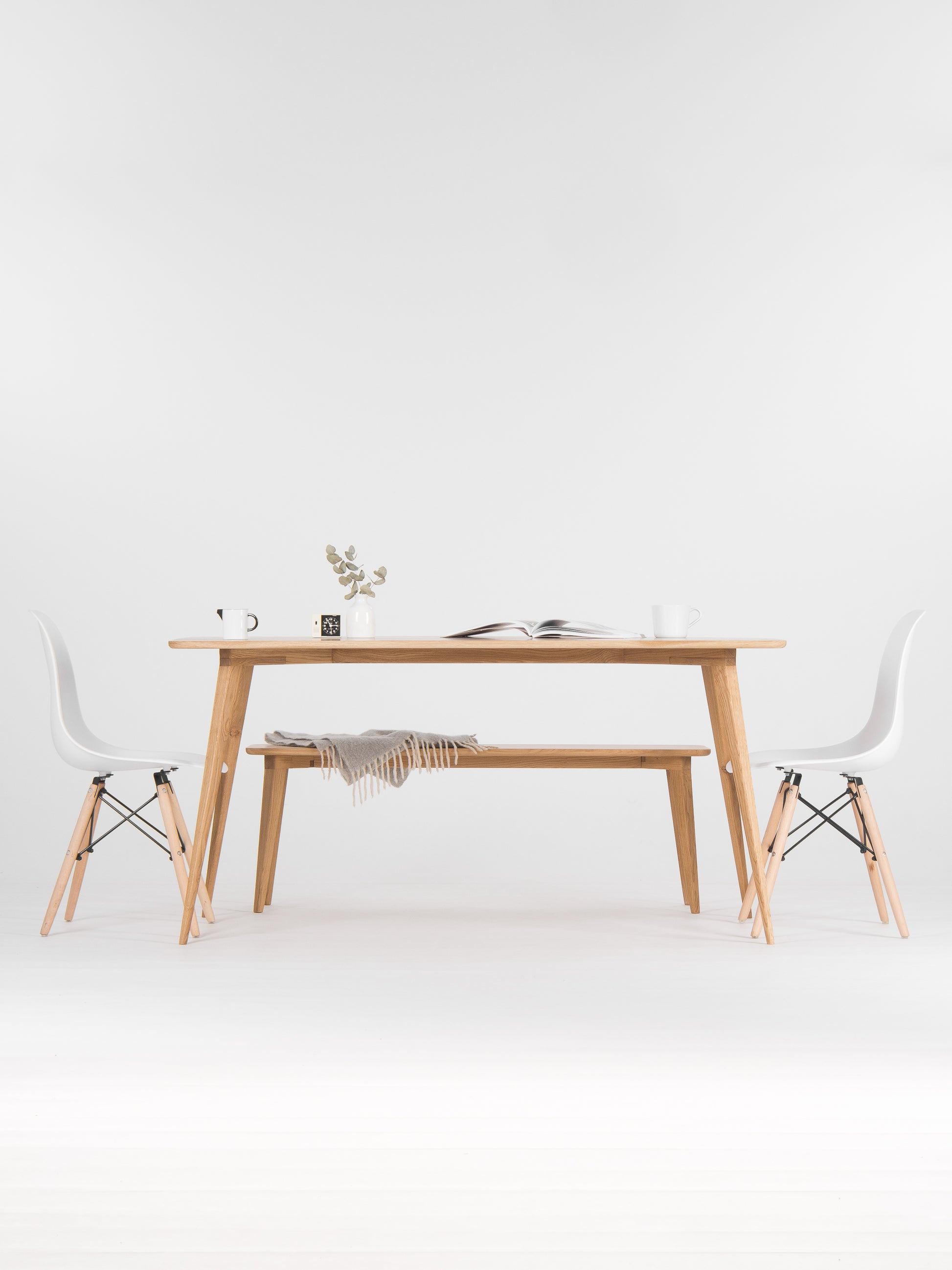 Minimalist dining area with a wooden table, chairs, a vase, and an open book.