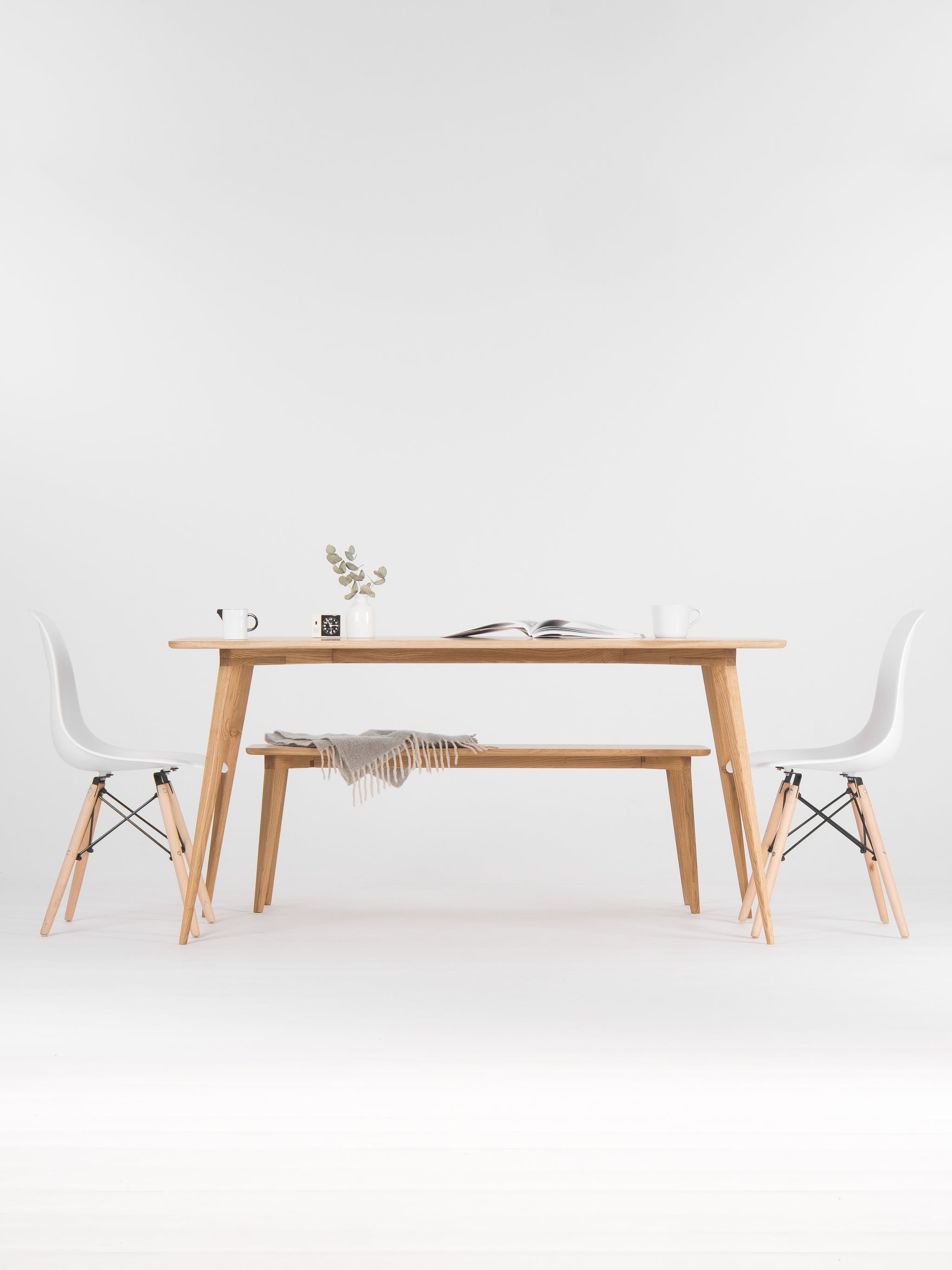 Minimalist dining area with a wooden table, chairs, a vase, and an open book.
