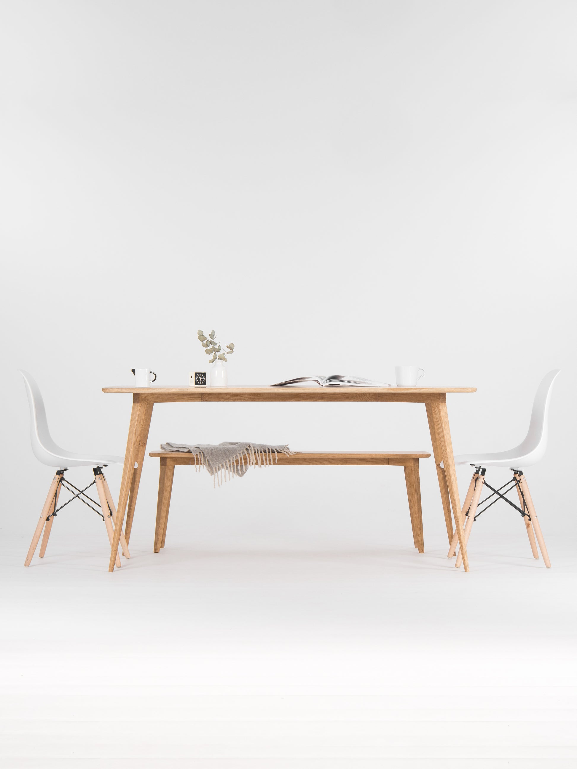 Minimalist dining area with a wooden table, chairs, a vase, and an open book.